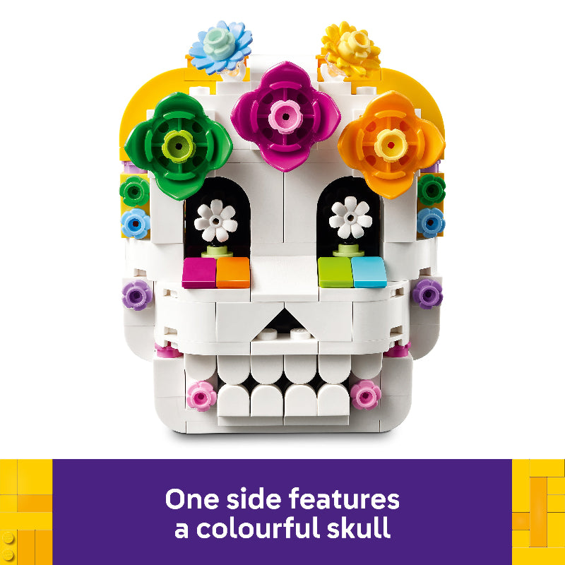 A white LEGO-style sugar skull toy with colorful floral decorations on a white background, plus a purple text banner at the bottom that reads, 'One side features a colorful skull.'.
