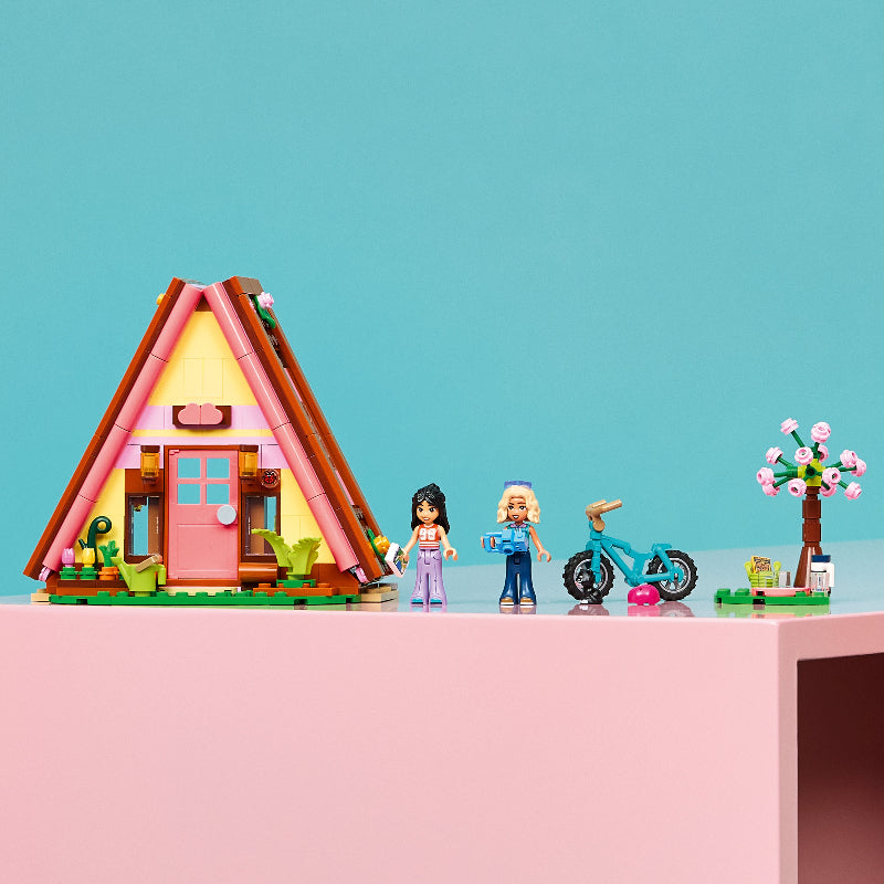 Colorful toy house with two dolls and a bicycle on a pink platform against a blue background