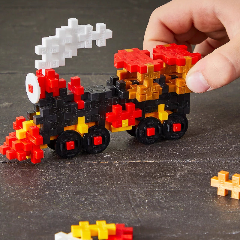 Hand building a pixelated car model with colorful blocks on a dark surface