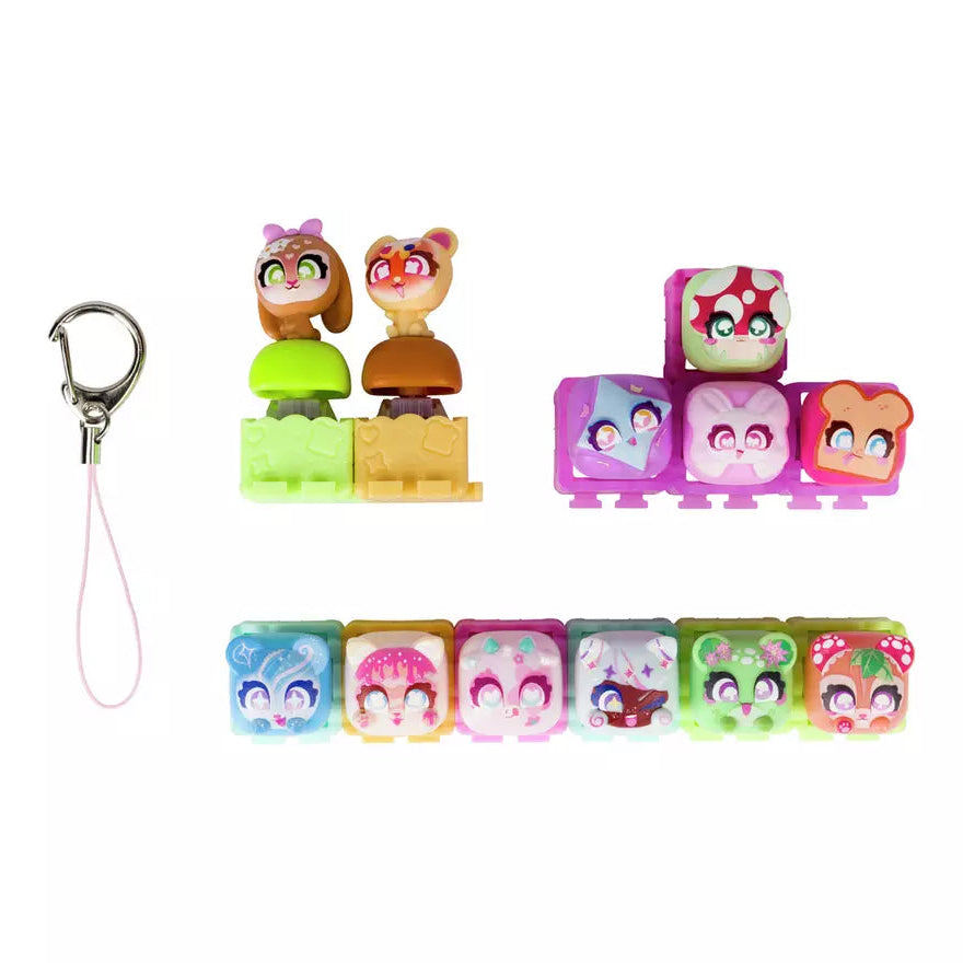 A set of colorful character-shaped plastic keychain charms and small accessory pieces on a plain white background. The set includes a silver key ring with a pink loop, two small character figures on green and tan blocks, a stack of pink and purple character pieces, and a row of six square charms with cartoon faces in blue, pink, white, green, and red.