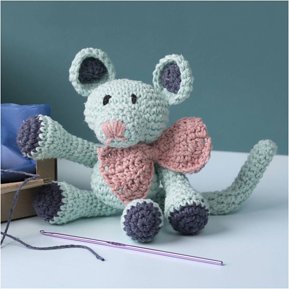 Crocheted mouse toy with a pink bow tie on a white surface with a blue background