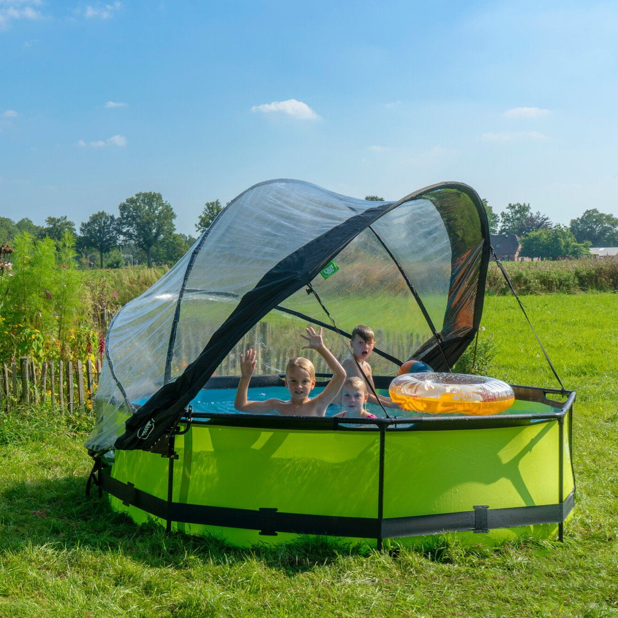 Children playing in a green inflatable pool with a canopy in a grassy outdoor setting.