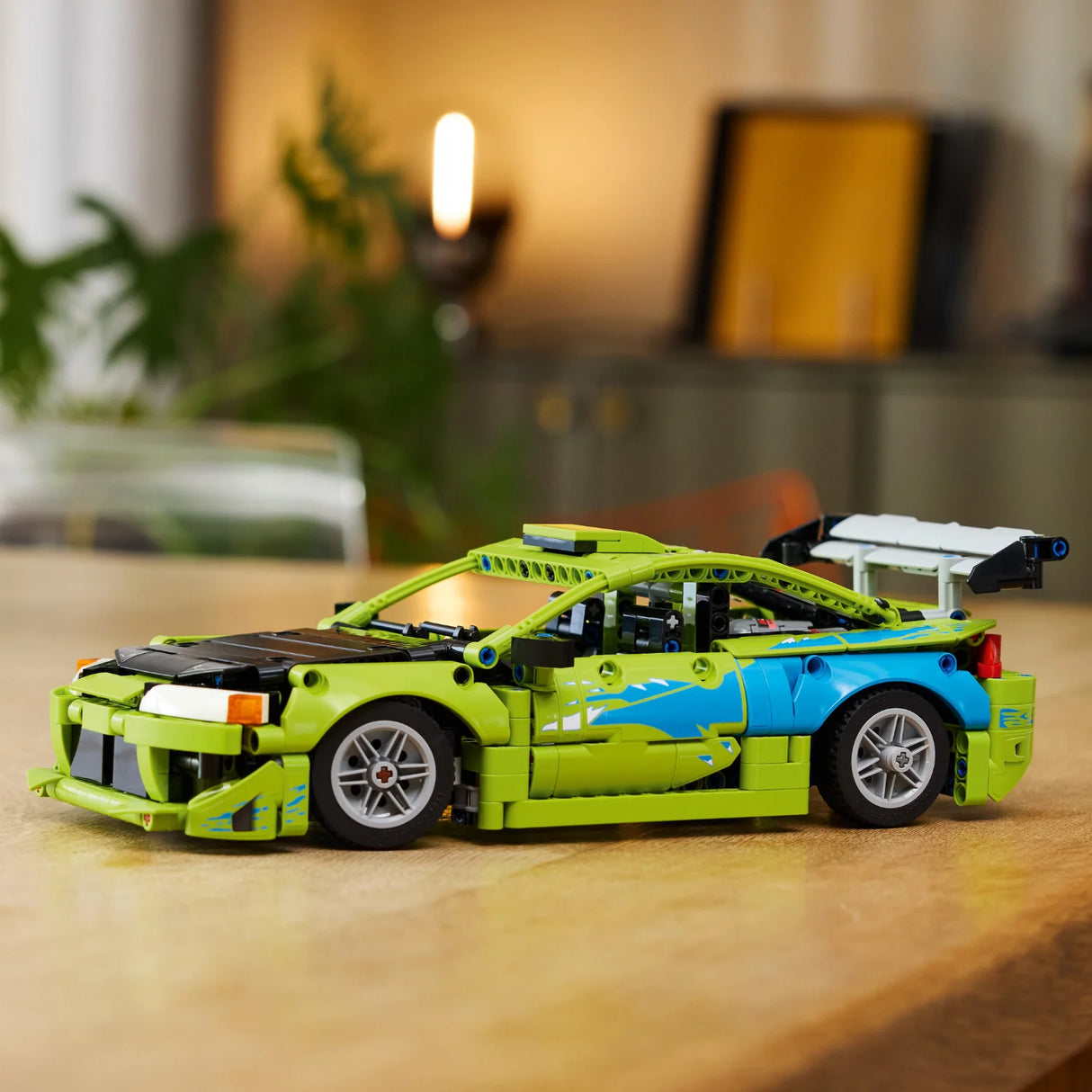 Green and blue toy car model on a wooden surface with a blurred indoor background
