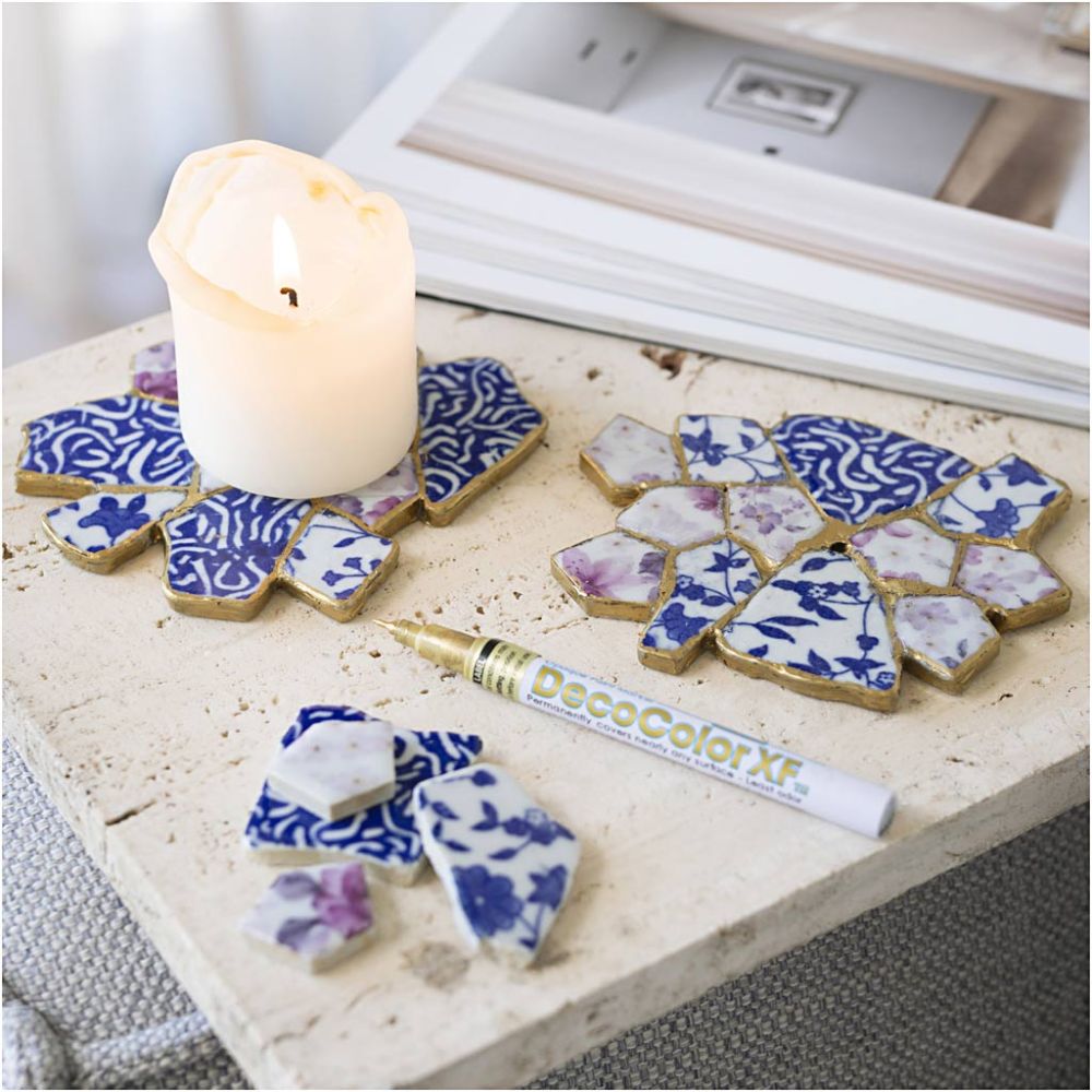 Decorative coasters with blue and white patterns on a surface with a candle and DecoColor XT tube.