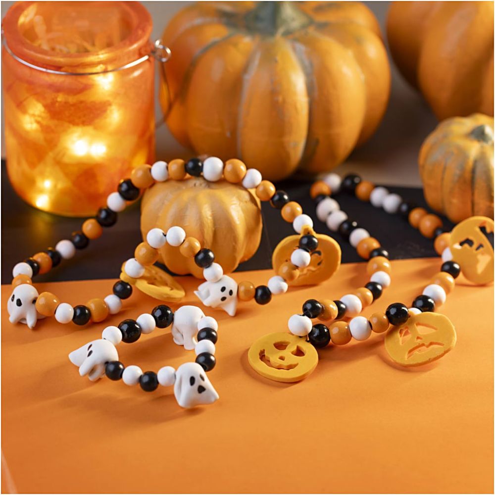 Halloween-themed beaded bracelets with ghost and pumpkin charms on an orange surface with pumpkins and a candle in the background.