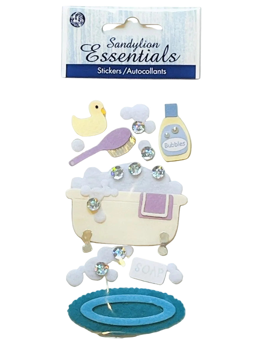 Sandylian Essentials bath-themed stickers in a clear plastic package with a blue header card. The stickers include a yellow duck, purple brush, bubble bottle, cream bathtub with purple towel, white clouds, rhinestones, and teal and blue oval shapes.