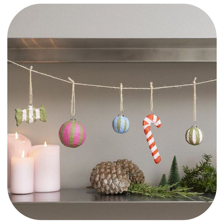 homemade christmas decorations hanging on a string over a shelf with candles, pinecones and green foliage