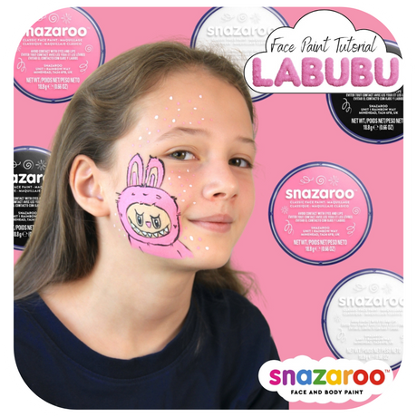 A girl with a pink labubu monster painted on her face on a pink background with Snazaroo face paint pots