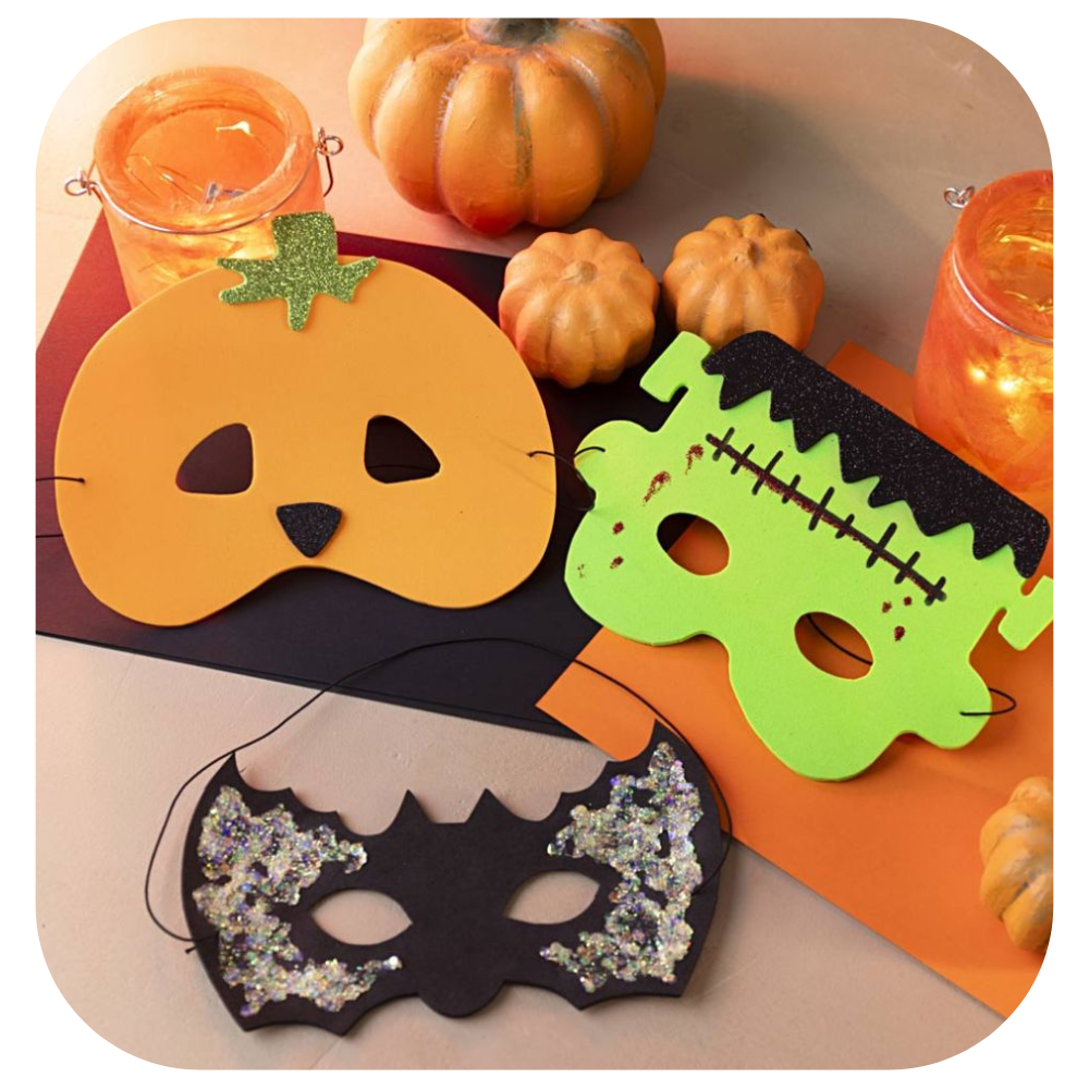 A picture of 3 foam homemade Halloween masks of a pumpkin, a monster and a bat on a table with other pumpkins and candles.