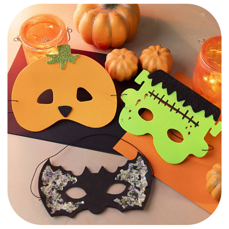 A picture of 3 foam homemade Halloween masks of a pumpkin, a monster and a bat on a table with other pumpkins and candles.