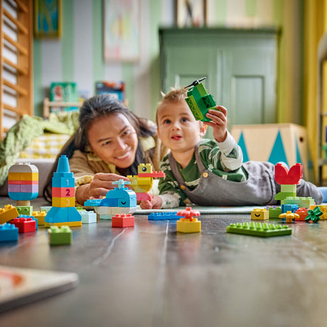 Child and adult playing with colorful building blocks on a table in a room.