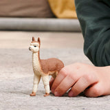 Toy llama figure on a textured surface with a hand interacting with it