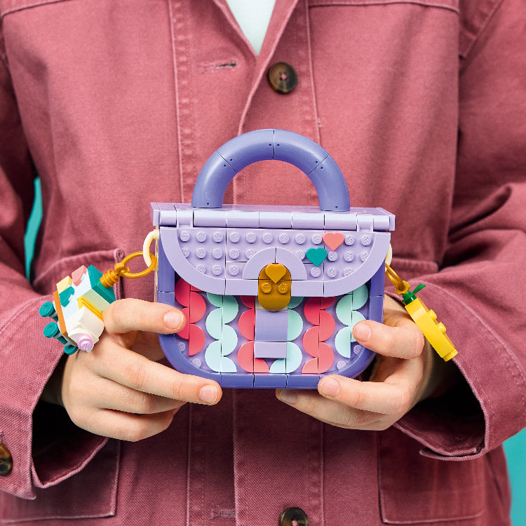 Person holding a colorful handbag made of interlocking bricks against a pink jacket background