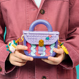Person holding a colorful handbag made of interlocking bricks against a pink jacket background
