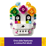 A white LEGO-style sugar skull toy with colorful floral decorations on a white background, plus a purple text banner at the bottom that reads, 'One side features a colorful skull.'.