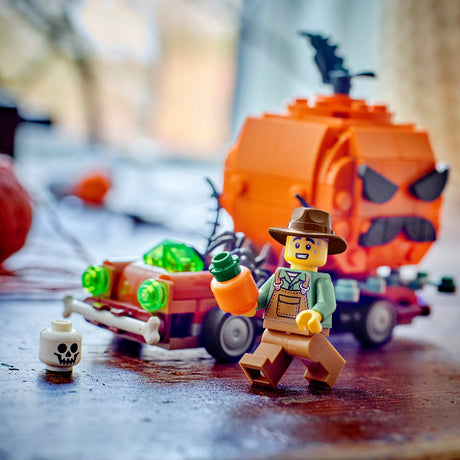 A LEGO minifigure dressed as a ghostly investigator stands beside a small red car with green translucent details and a large orange pumpkin head on a dark tabletop. The scene is softly blurred in the background.