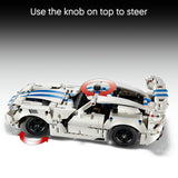 A white and blue building-block toy sports car shown on a gray gradient background with instructional text at the top reading 'Use the knob on top to steer' and red arrow graphics indicating steering.