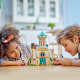 Two children playing with a toy castle on a table.