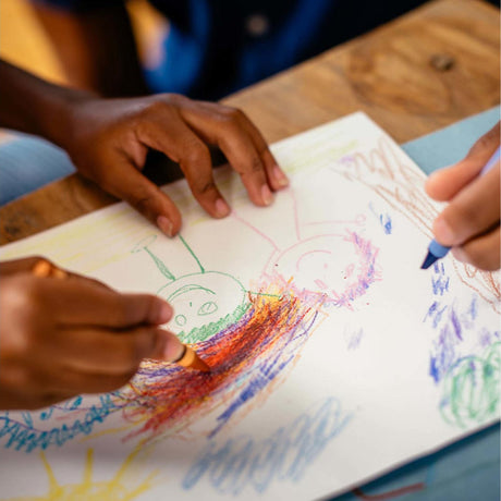 Children's hands coloring a drawing of a sun and a tree on a piece of paper.