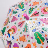 A clear plastic umbrella with a colorful cartoon forest print, featuring owls, birds, trees, mushrooms, and animal illustrations. The handle is pink, and the umbrella is shown open against a light gray background.