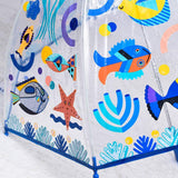 A clear plastic umbrella with a colorful underwater theme print, featuring cartoon fish, a starfish, and sea plants on a white background.