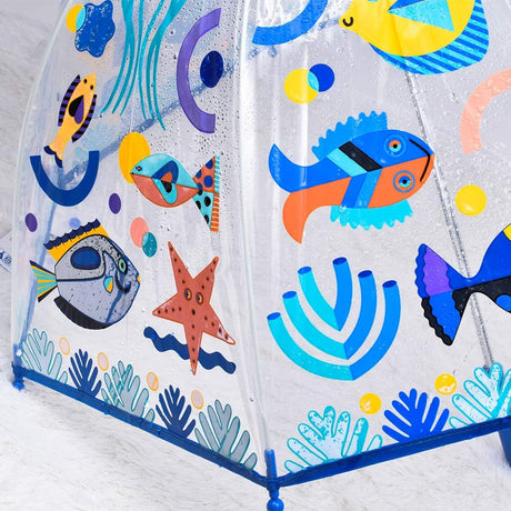 A clear plastic umbrella with a colorful underwater theme print, featuring cartoon fish, a starfish, and sea plants on a white background.