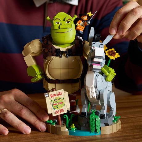 LEGO Shrek and Donkey set with a person assembling the figures on a wooden surface.