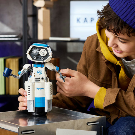Child playing with a robot toy in a room with a bookshelf and computer monitor in the background.