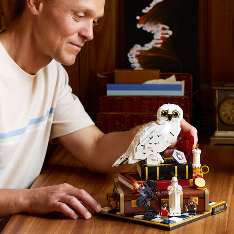 Man holding a LEGO owl on a table with a detailed LEGO set in the background