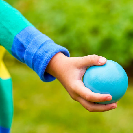 Child's hand holding a blue ball with a green blurred background