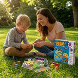 A woman and a young boy sitting on a grassy lawn outdoors, playing with a colorful bee-themed board game. The product box labeled 'Bee' is standing next to them on the grass.