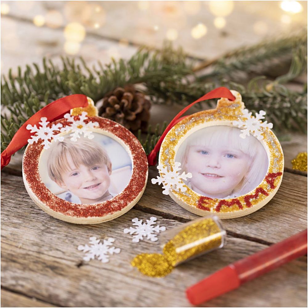 Two Christmas ornaments with pictures of children on a wooden surface with festive decorations.