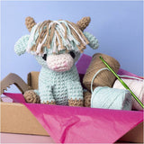 Crocheted cow with yarn and a crochet hook on a pink surface