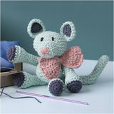 Crocheted mouse toy with a pink bow tie on a white surface with a blue background