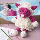 Crocheted pink sheep on a pink table with yarn in the background