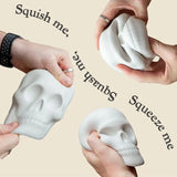 Four hands demonstrate different ways to squeeze and squish a white skull-shaped squishy toy against a solid beige background, with text reading 'Squish me', 'Squeeze me', and 'Squish me,'.