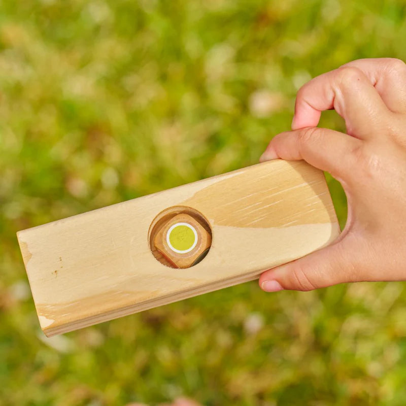 Hand holding a wooden tool with a circular component against a blurred green background