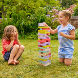 Two children playing with a tall tower of colorful wooden blocks in a garden.