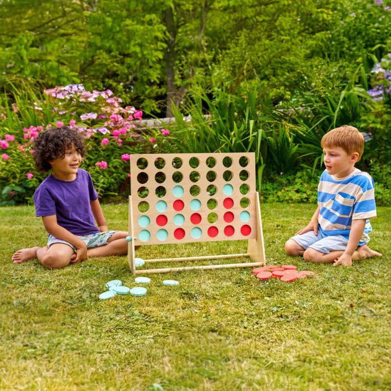 Two children playing with a large outdoor connect-four game in a garden.