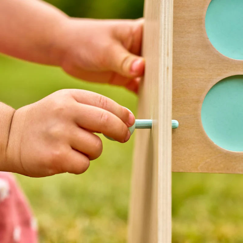 Child's hand using a screwdriver to interact with a wooden toy outdoors.