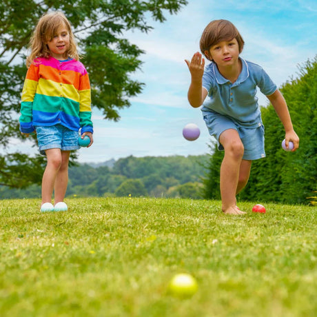 Two children playing with balls on a grassy field.