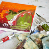 Art supplies including oil paints and a painting on an artist's table.