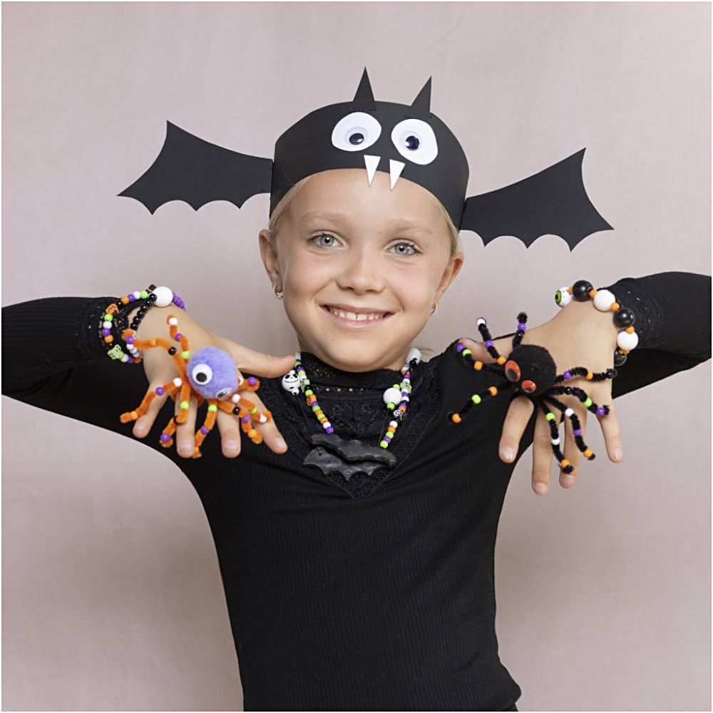 Child in a bat costume with spider decorations on a plain background