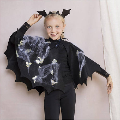 Child wearing a black bat costume with wings and headpiece on a plain background