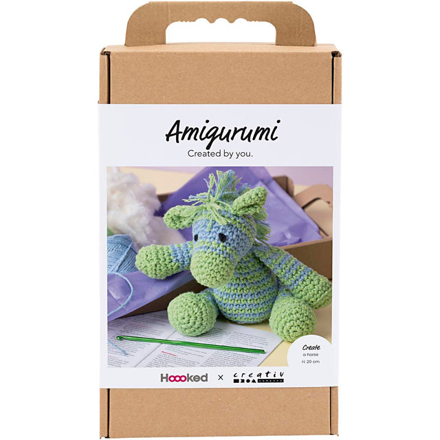 Amigurumi crochet kit packaging with a green and blue plush toy, hoop, and yarn on a white background.