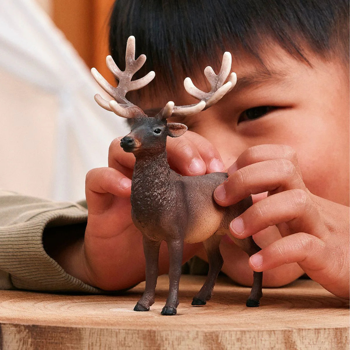 Child holding a small deer figurine on a wooden surface