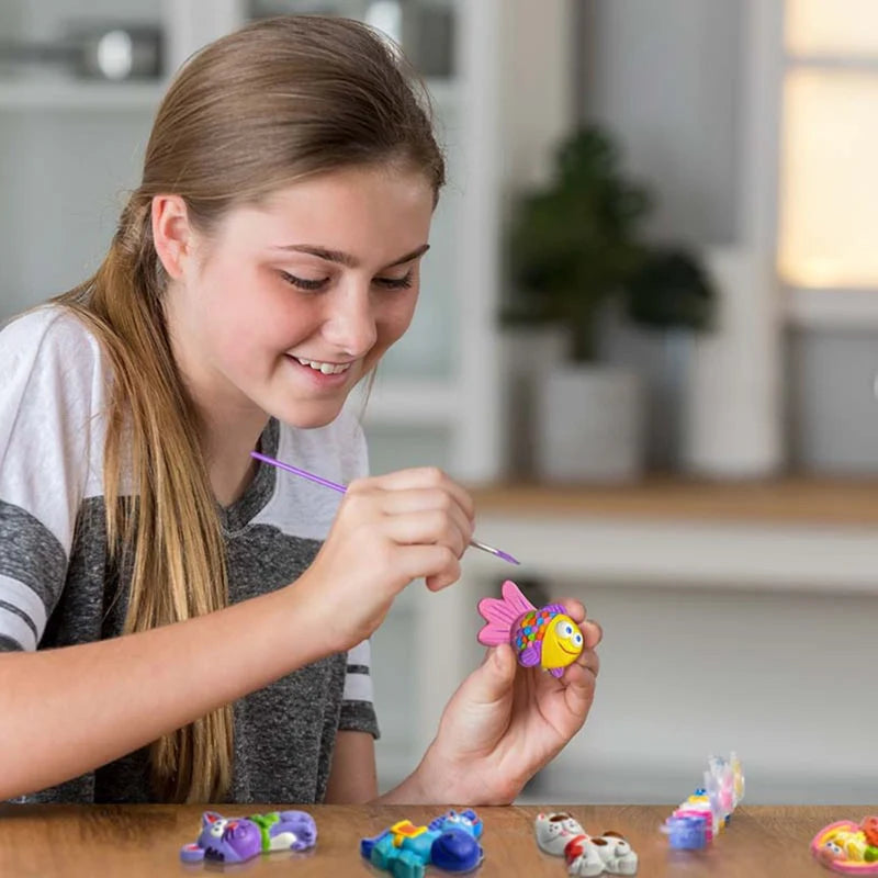 Young girl painting a small figurine with a brush in a home setting