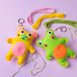 Two colorful felt animals that were stitched as a craft project, one yellow and one green, on a purple background.