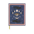 A hardcover journal with a dark blue cover featuring an intricate celestial illustration of a central eye, moon phases, stars, and dark birds, framed by a pink border. A gold ribbon bookmark is visible at the bottom.