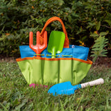 Colorful gardening tools in a green and blue bag on grass with plants in the background